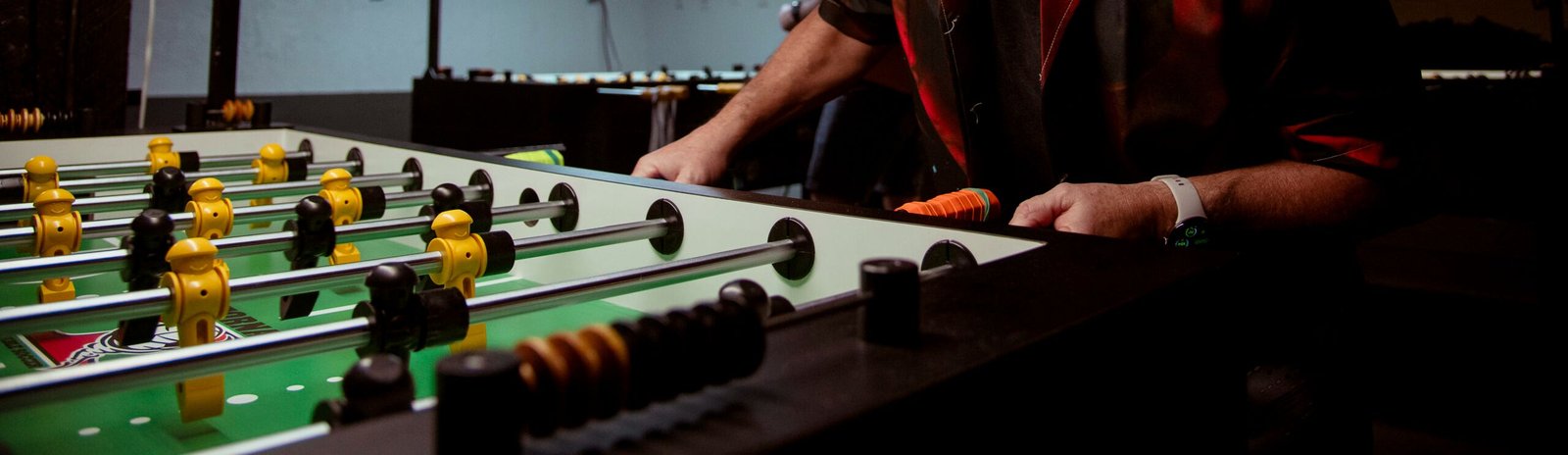 Alquiler de futbolines en León Persona jugando al futbolín en interior iluminado.